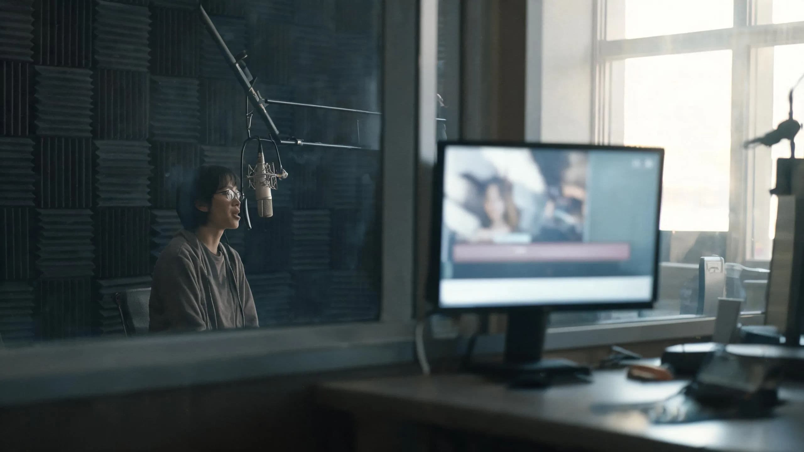 A voice artist in a booth while a producer pairs the brand clip with captions