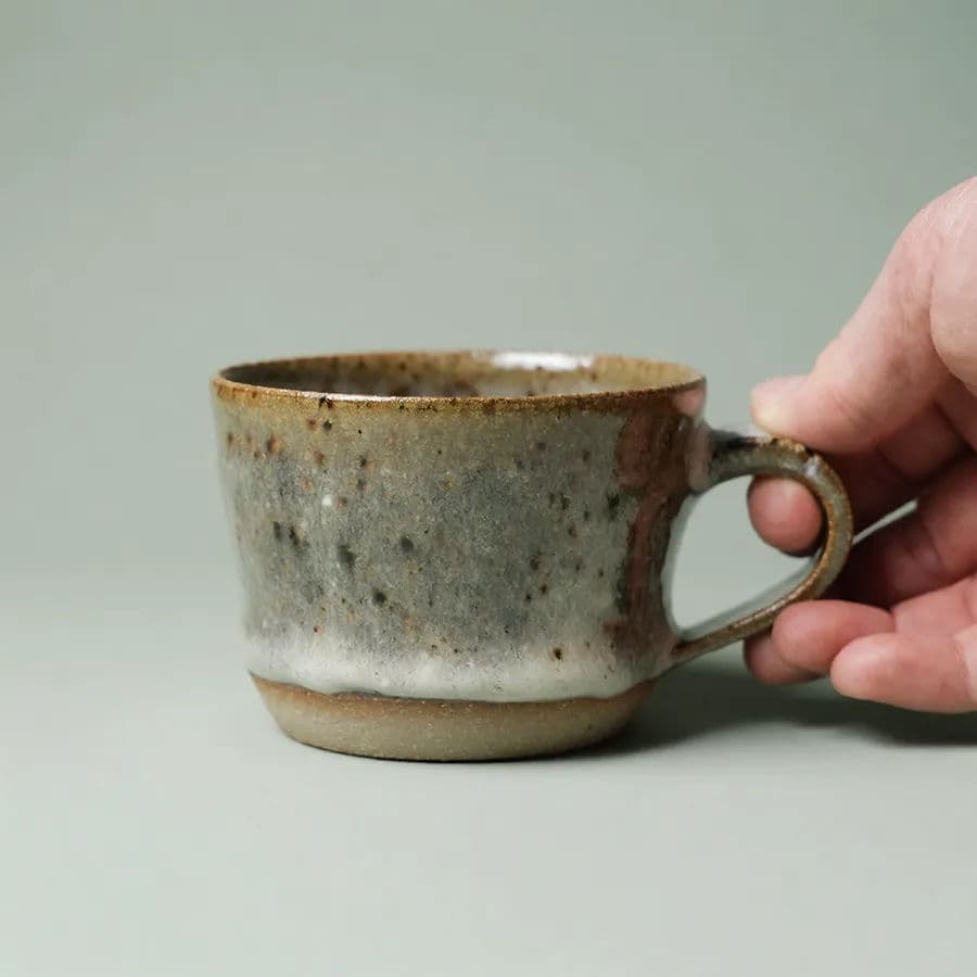 The same speckled handmade mug held in one hand to show its size