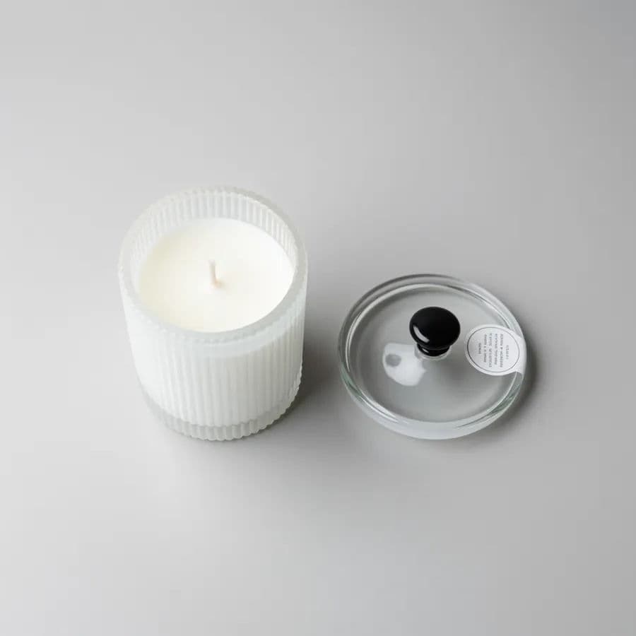 Plain studio cutout of a white ribbed jar candle on a light background