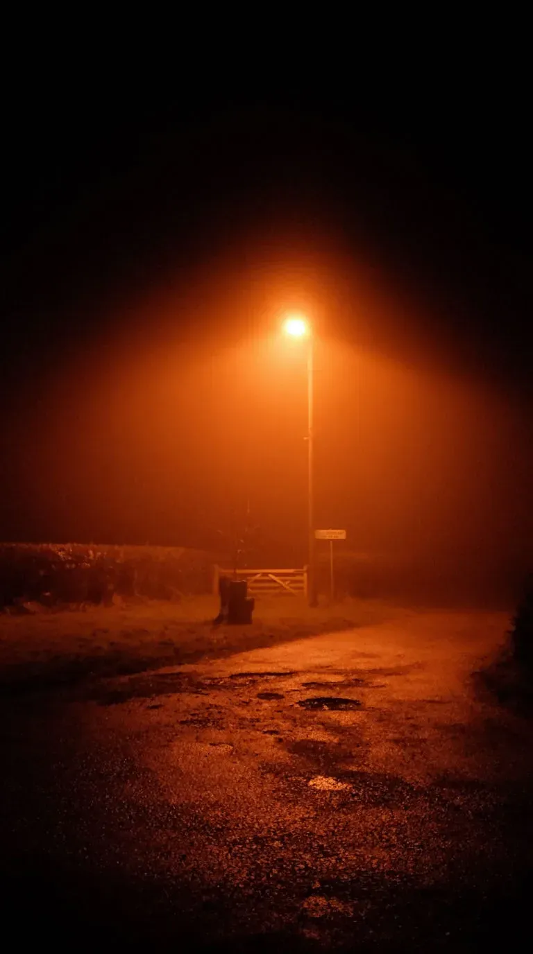 A single sodium streetlight glowing orange in thick fog on an empty country lane at night, generated with Krea 2 Large