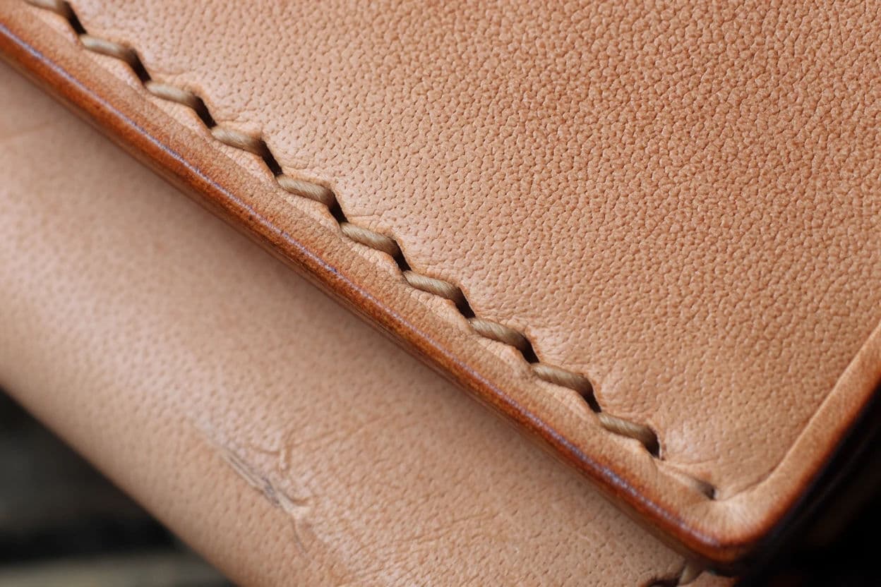 Macro of leather grain on a wallet edge with visible stitch holes, generated with Krea 2 Large