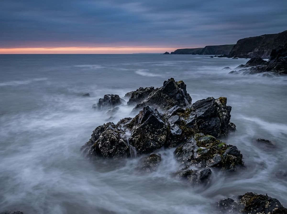 Coastal landscape photograph with a long exposure turning breaking surf into low mist around dark rocks, generated with Nano Banana 2