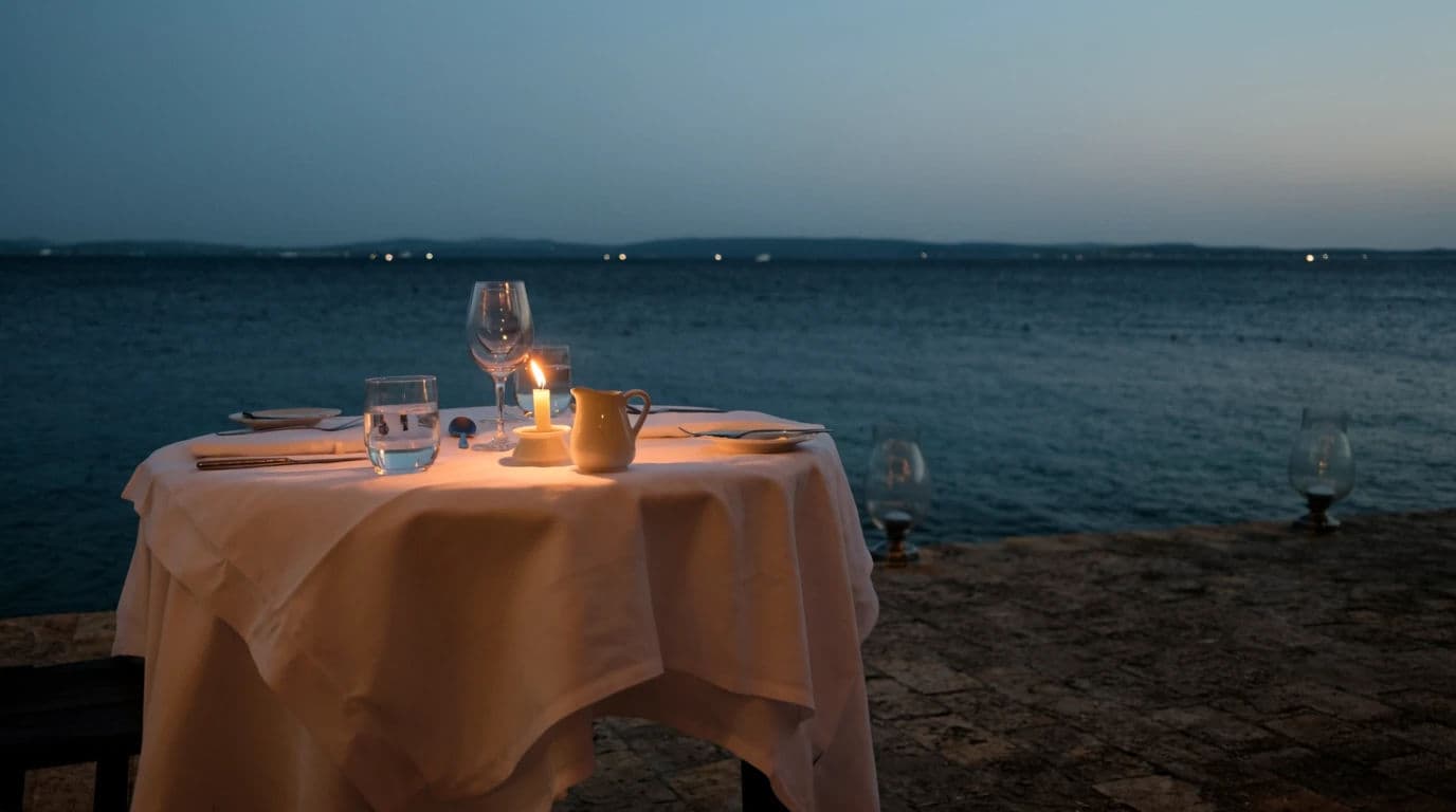 Wide photograph of a hotel terrace table laid for two overlooking dark water at dusk, generated with Krea 2 Large