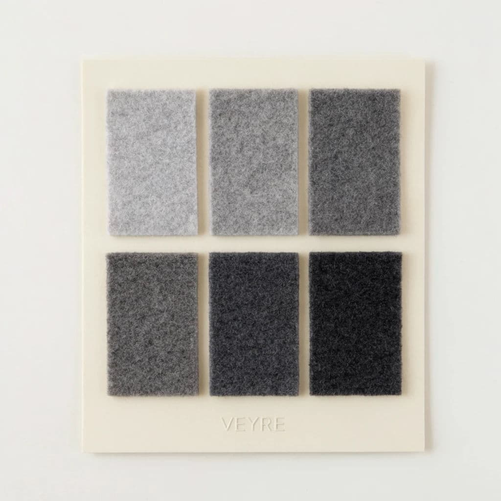 Square photograph of a material swatch card holding six grey wool samples with a debossed house name, generated with Krea 2 Large