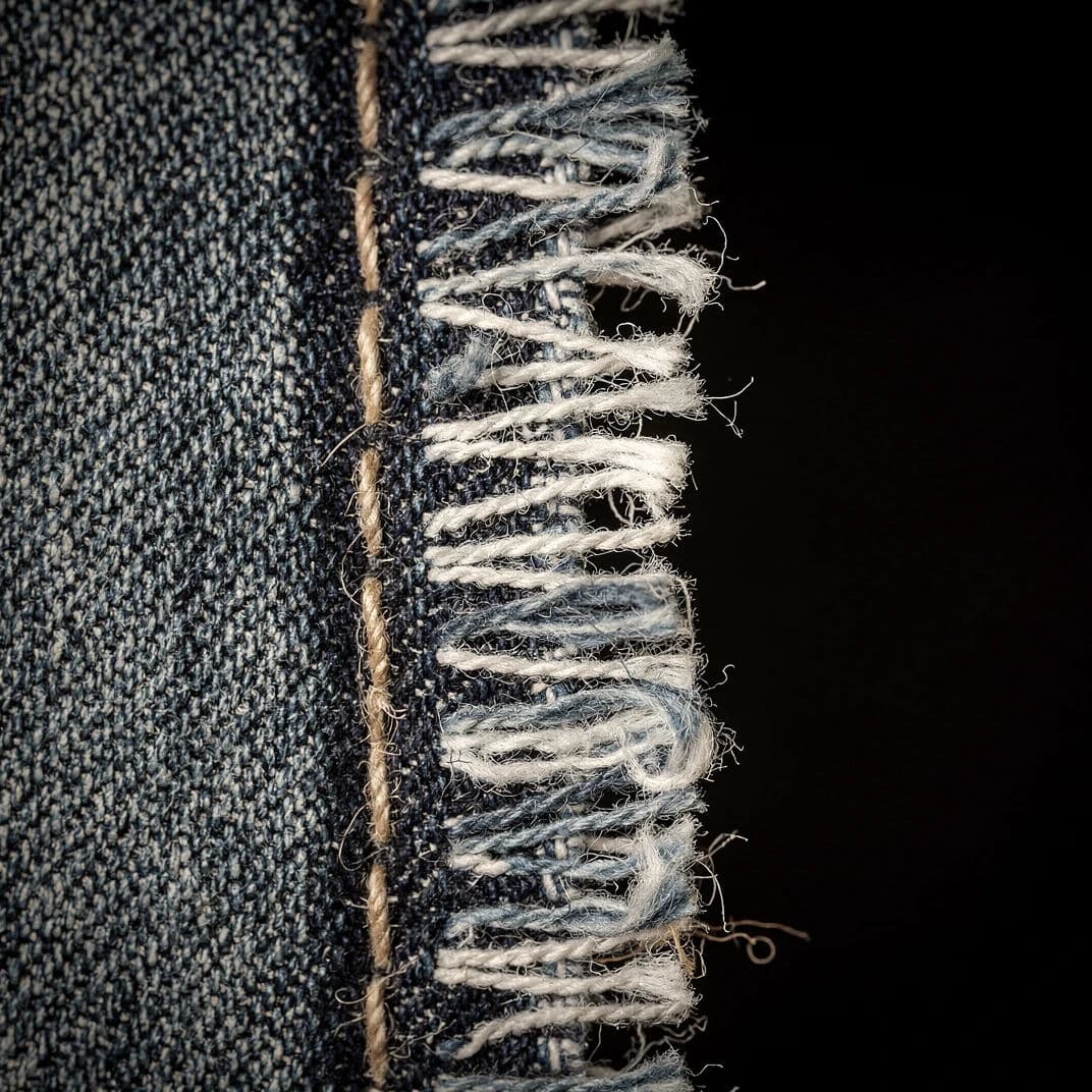 Square macro photograph of a frayed denim edge showing the warp and weft threads separating, generated with Flux 2 Pro