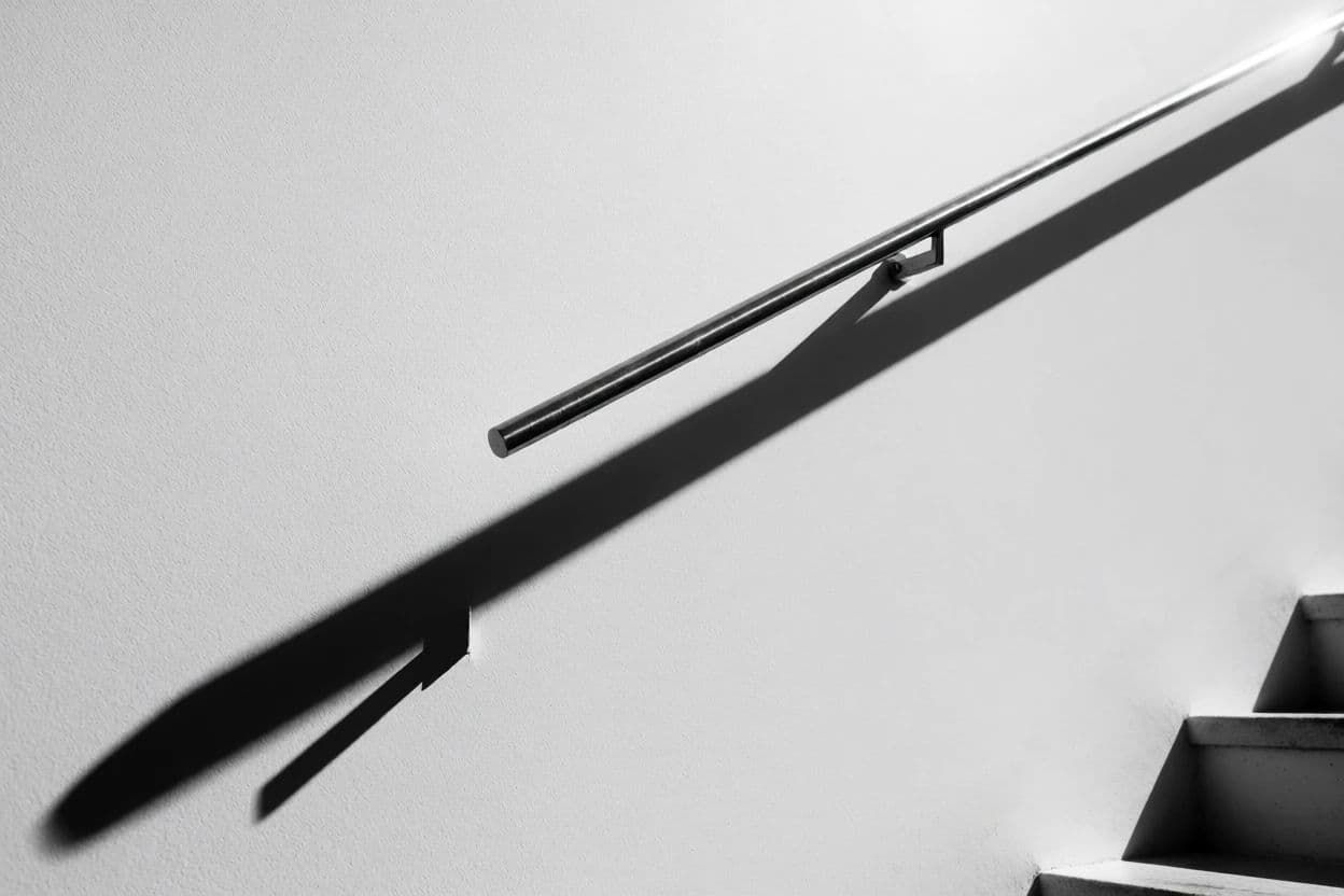 Photograph of a stair handrail casting a long clean shadow across a white wall, generated with Krea 2 Medium