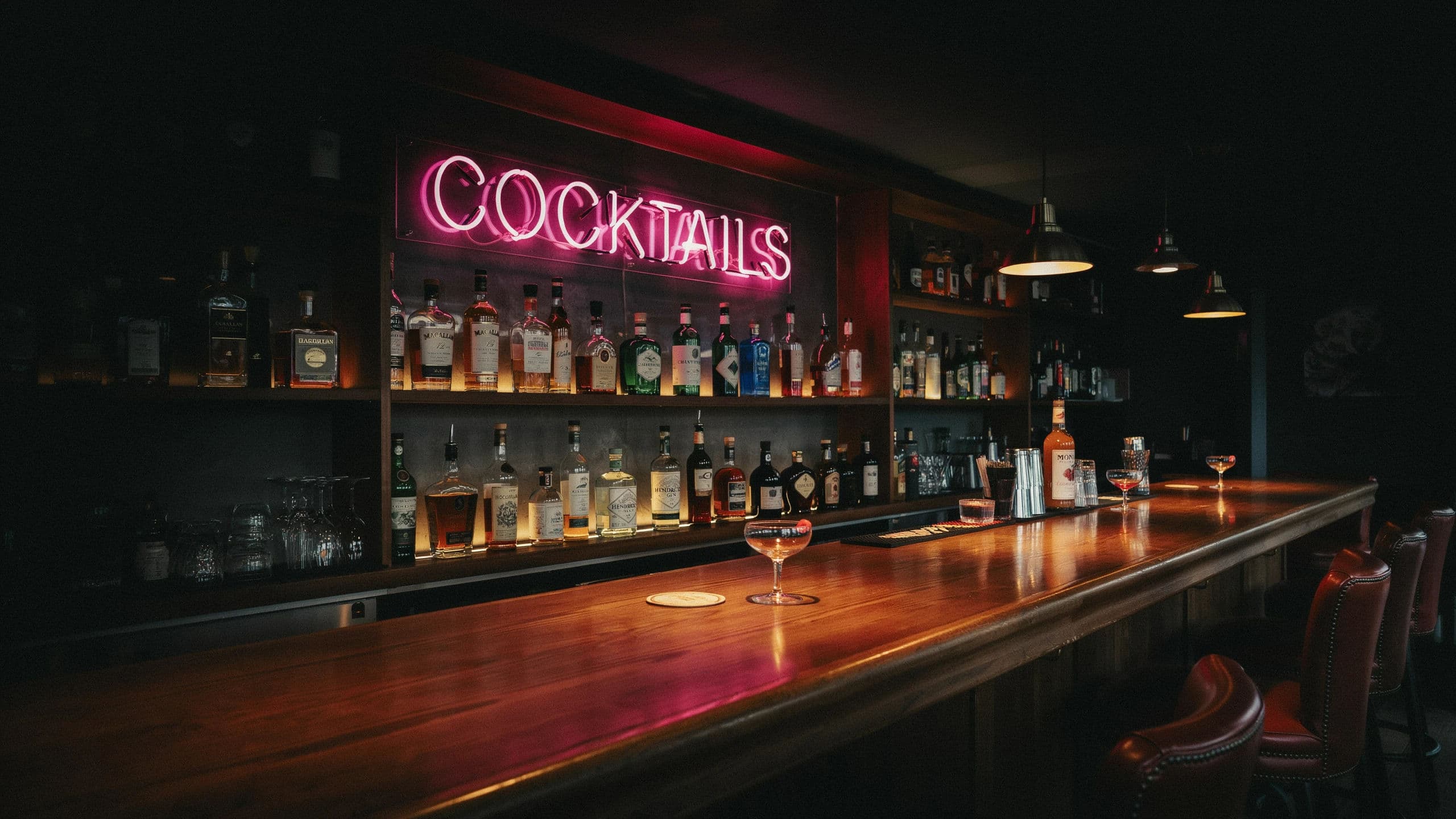 Wide photograph of a bar back lit by a pink COCKTAILS sign mounted above the bottles, generated with Ideogram 4.0