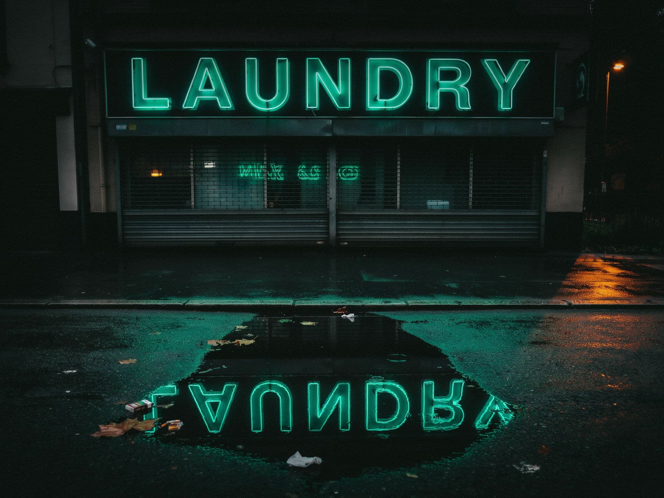 Photograph of a LAUNDRY sign reflected whole in a puddle on the pavement below it, generated with Ideogram 4.0