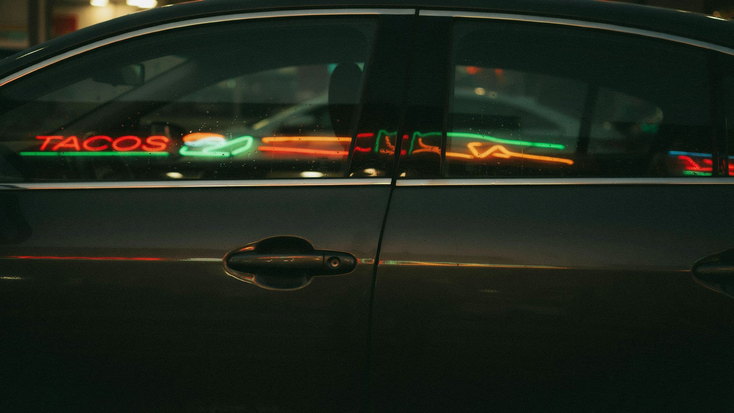 Wide photograph of a row of neon shopfronts reflected along the side glass of a parked car, generated with Ideogram 4.0