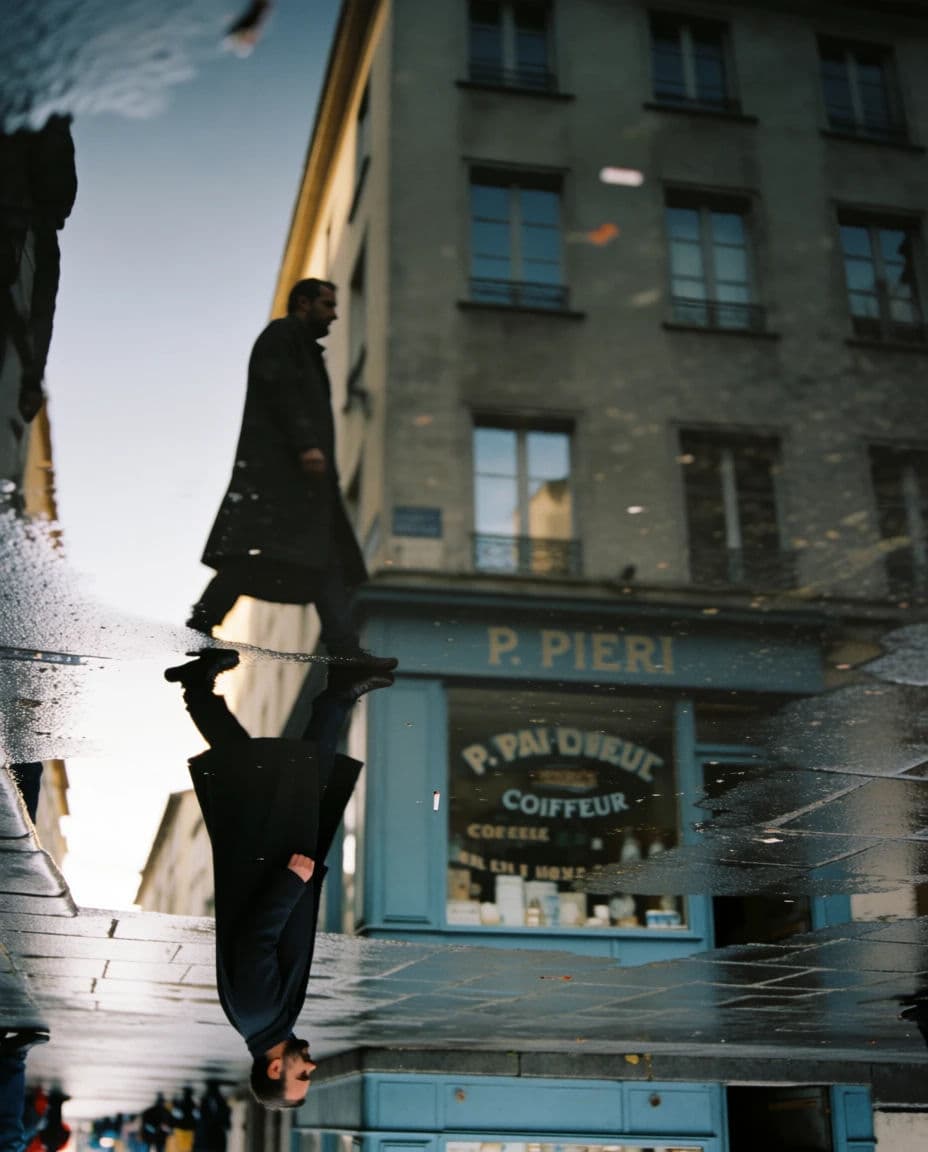 Street photograph of a large puddle returning the full height of the building above it, generated with Krea 2 Medium
